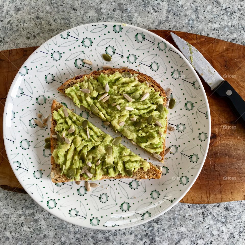 Avocado toast on seeded bread scattered with pumpkin and sunflower seeds and drizzled with olive oil