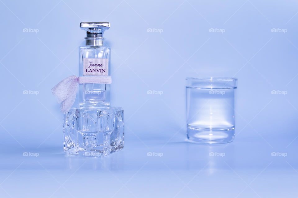 Eau de Parfum Lanvin pink on a blue background and a glass of clean, clear water.