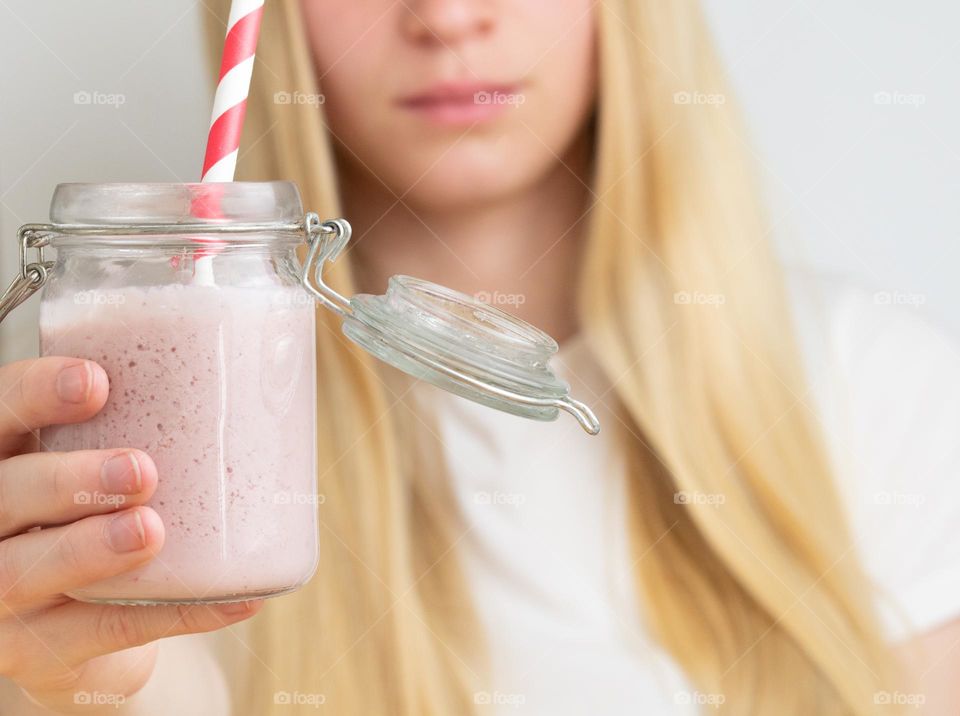 A blonde woman or girl holding a glass with strawberry milkshake or smoothie with straw 