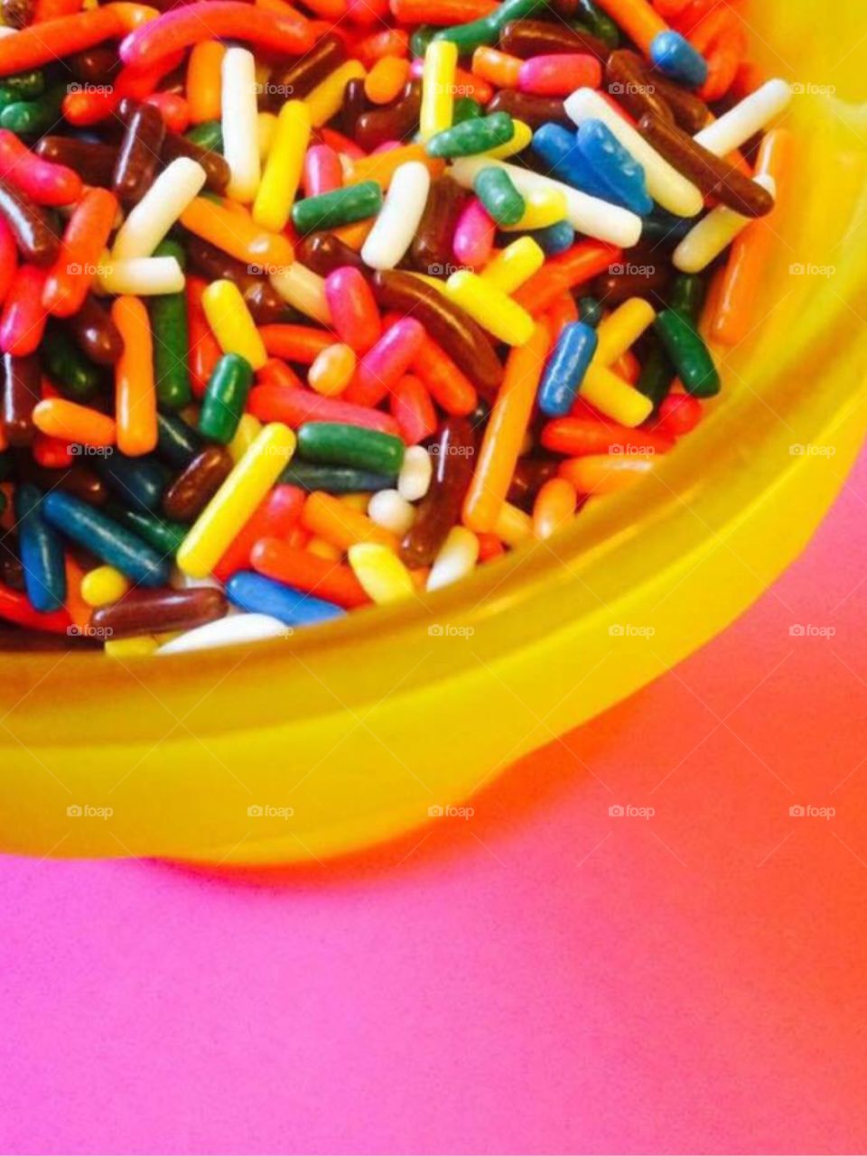 Rainbow Sprinkles in Dish. Colorful rainbow sprinkles in a yellow sorbet dish on a bright pink background