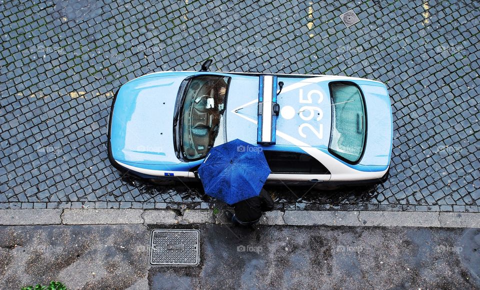 Rainy day blues . Overhead shot of a blue taxi with a blue umbrella on cobblestone streets in Rome