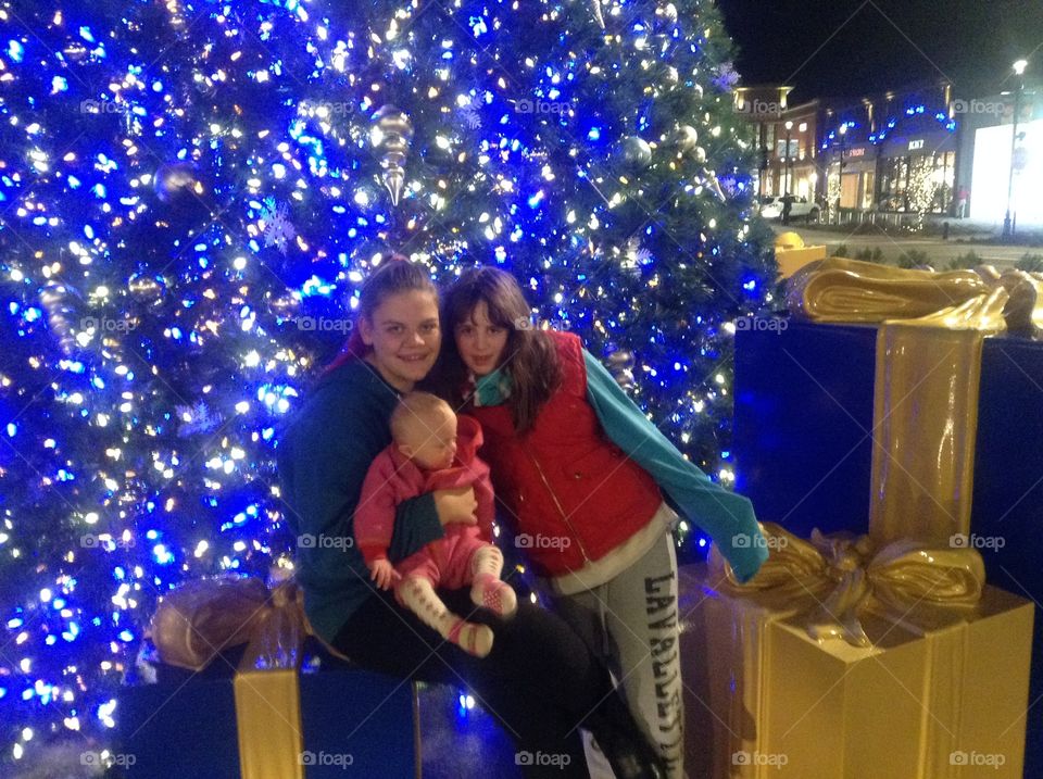 Siblings with baby sister with Down syndrome in front of blue and white Christmas tree