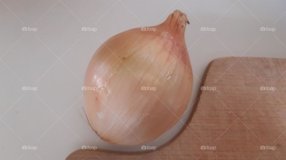 light brown golden (light ocher color) sugar onion lies near the edge of a wooden board on a cream-colored table
