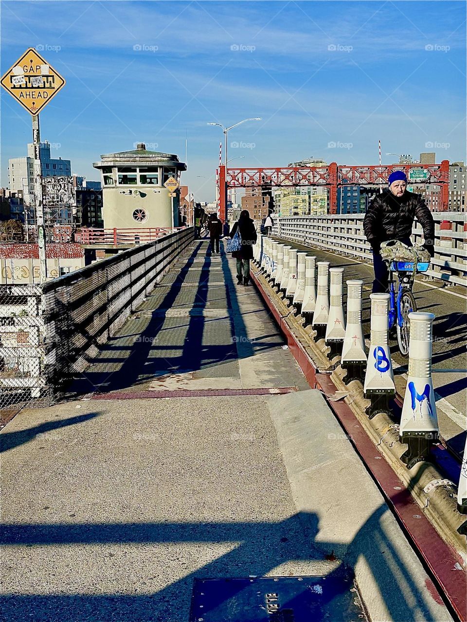 The bicyclist on the right exudes a determined sense of direction as he speeds along the bicyclist lane of the “Pulaski Bridge” towards “Greenpoint”, Bklyn. The lady in the pedestrian lane is walking towards LIC, Queens. 2023. Hypnotic Productions