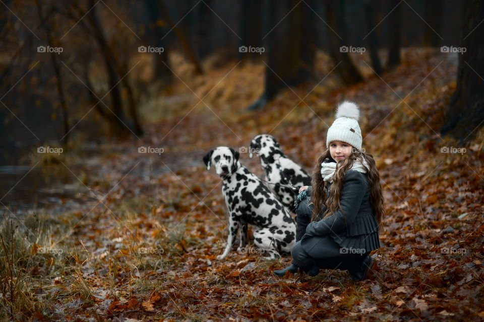 Little girl with Dalmatian dogs in autumn park 