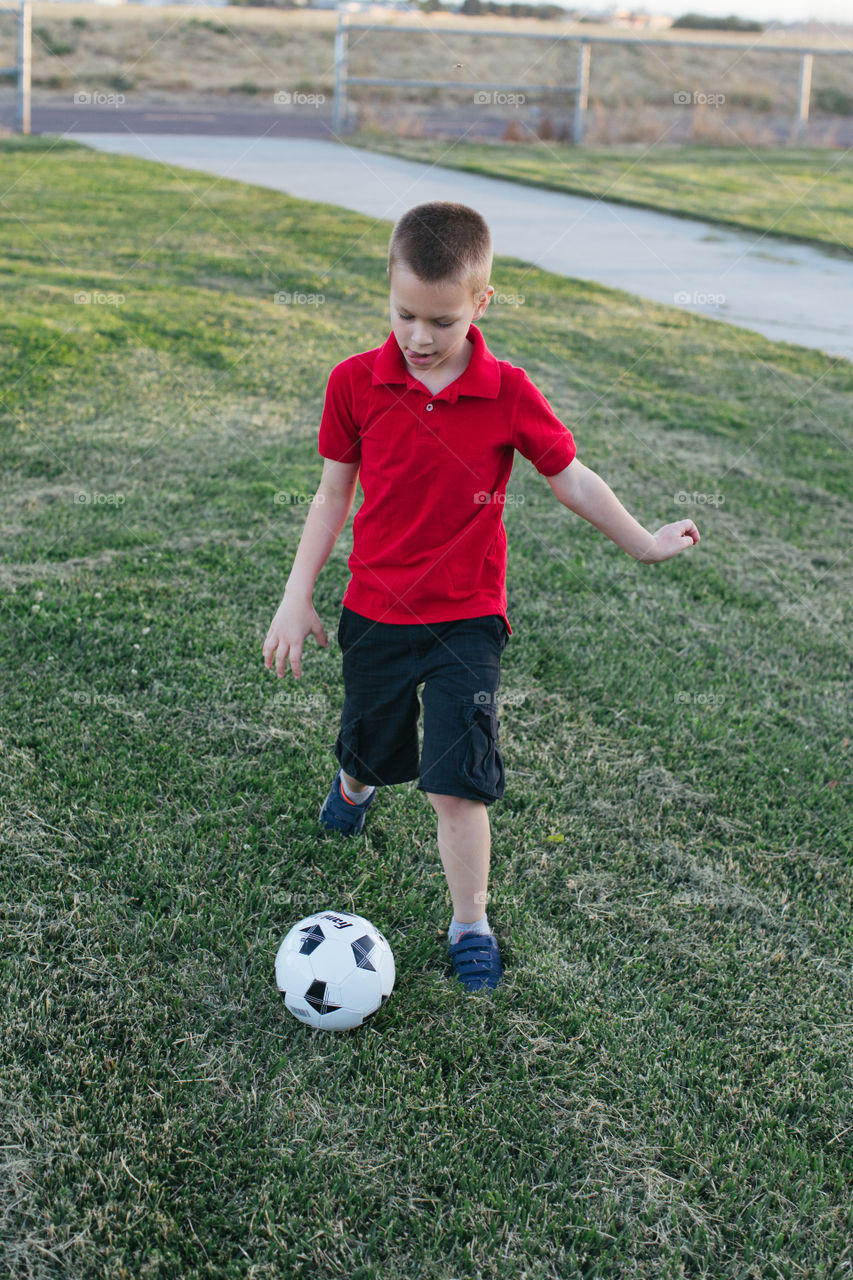 Six year old boy playing with soccer ball in park 