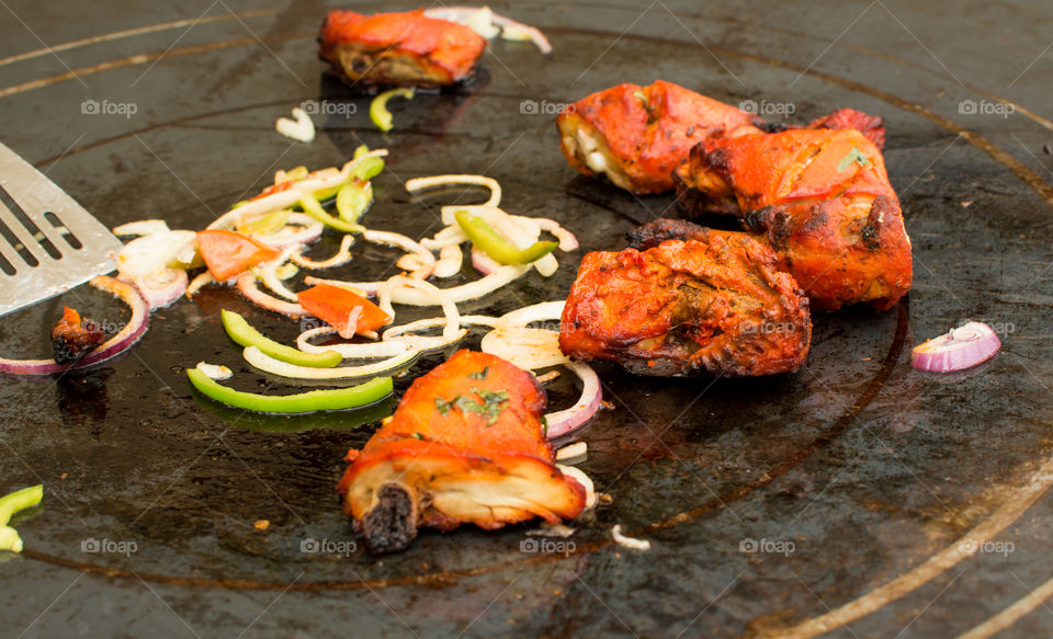 Cooking tandoori chicken on hot plate grill 