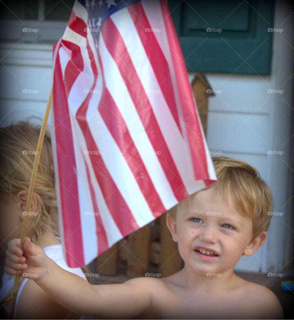 Two year old little boy gazing upwards at the American flag in his hand. 