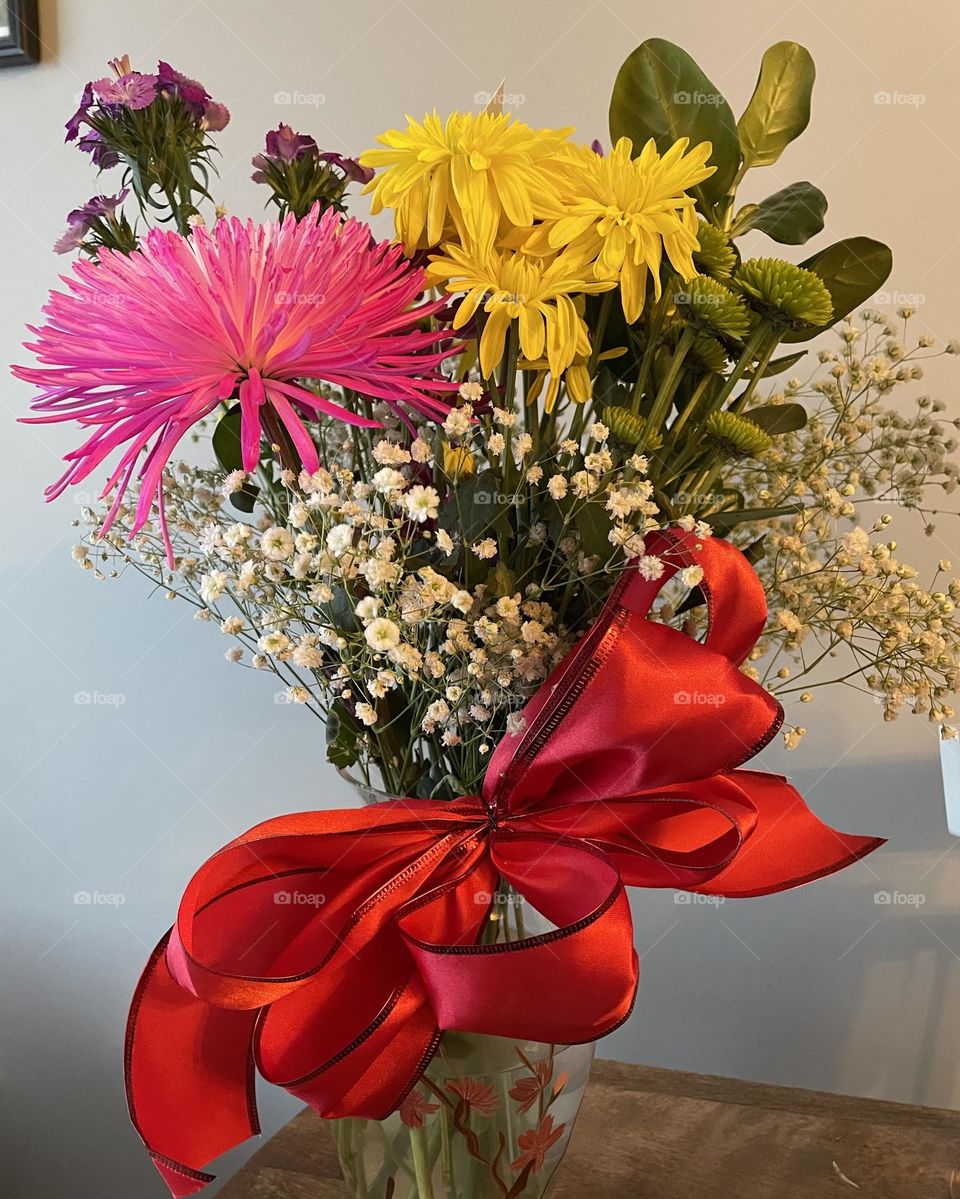 Flowers in a vase that I got for Valentines day, the vase is clear glass with flowers painted on, there was a big pink flower, some yellow ones, purple little ones, babies breathe (little white ones), some greenery, and a bright red ribbon bow