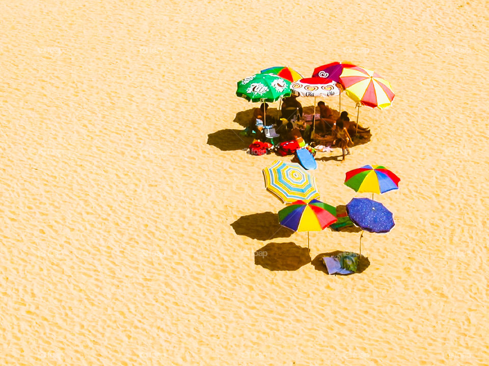 Viel Sand, viele Sonnenschirme, unter den Sonnenschirmen eine Gruppe Menschen