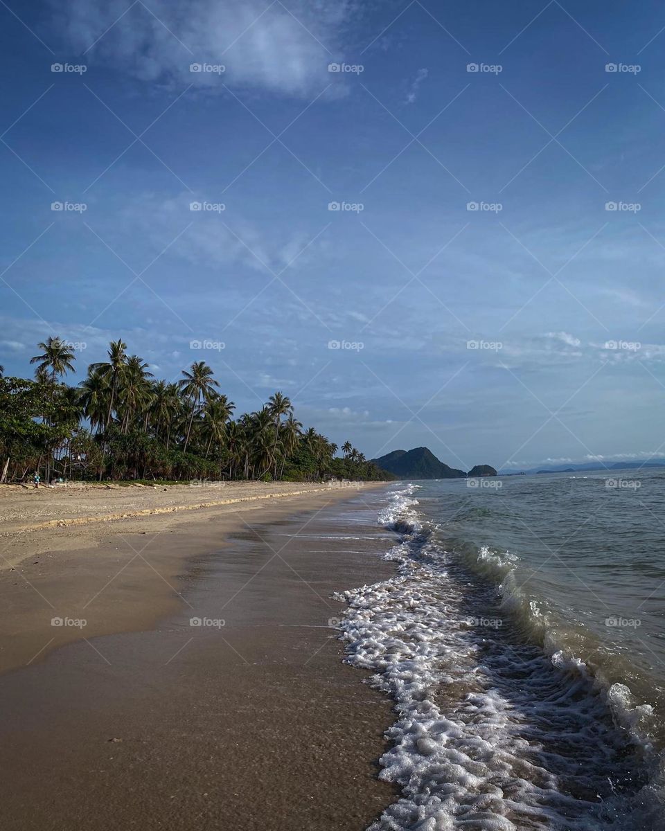 Small waves crashing on sandy beach with blue skies 