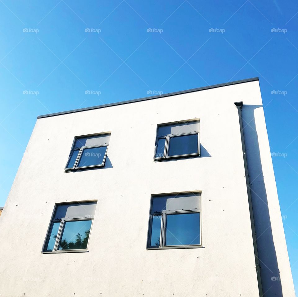 Minimal shot of White building with four windows against blue sky 