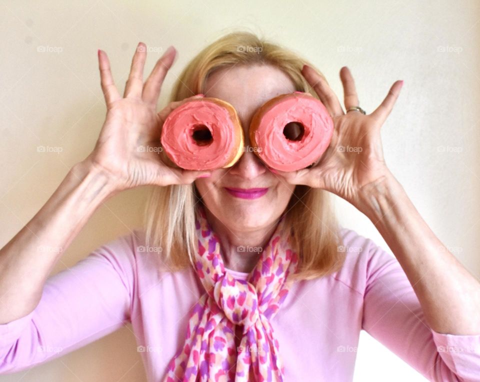Woman in pink holding pink donuts in front of her eyes selfie