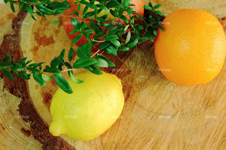Whole fruits: red apple, orange, orange, lemon yellow are on a wooden board, they are decorated with branches of myrtle.