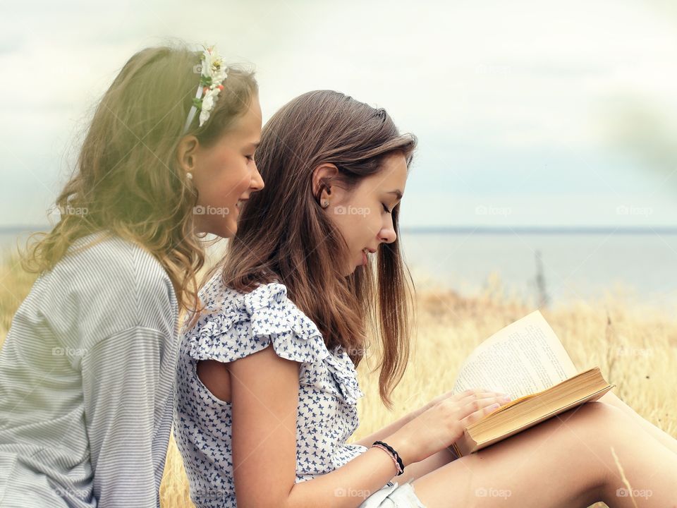 Two girls reading a book in the field 