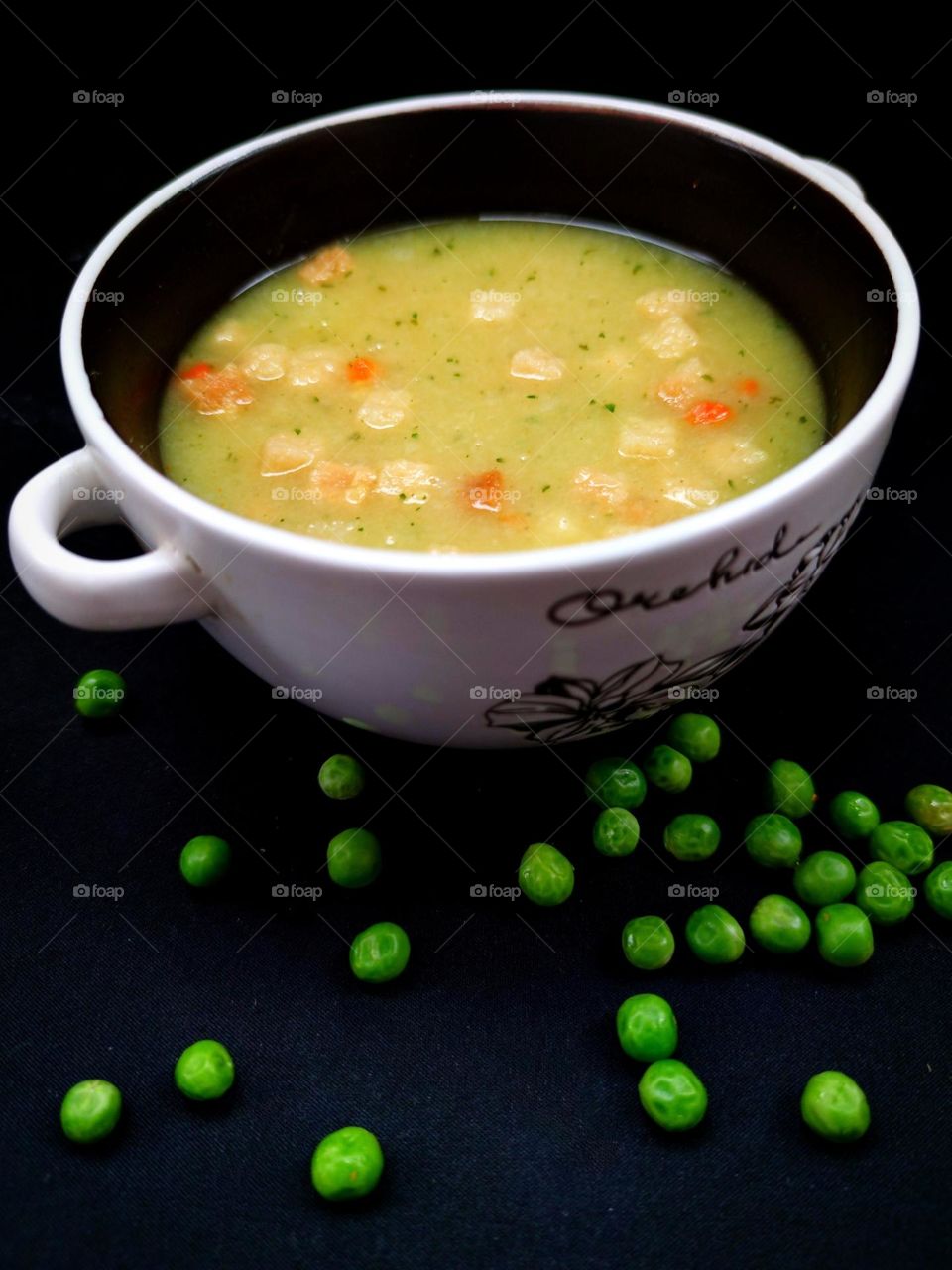 Food. On a black background is a deep plate. In a deep plate pea soup-puree with croutons. Green peas are scattered near the plate