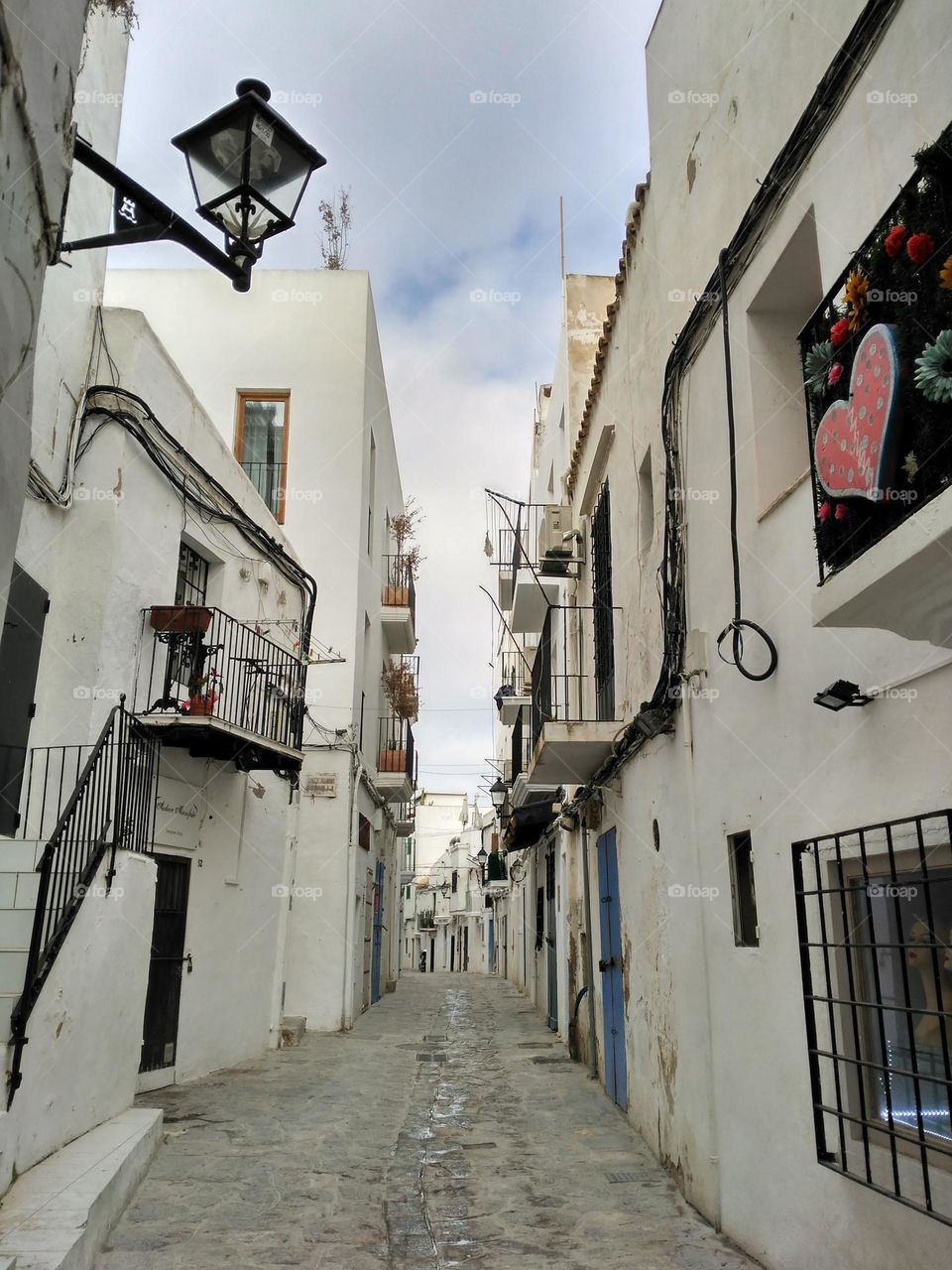 Side of typical buildings of Ibiza, Spain. Cobblestone streets with white buildings and black iron details such as stair railings and window bars.