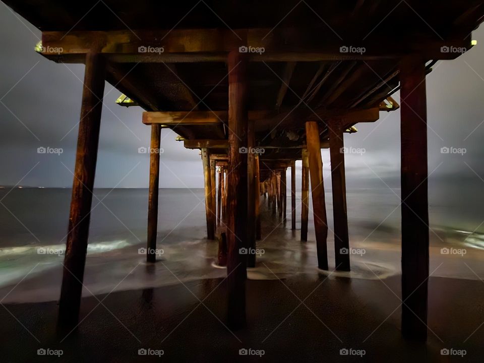 Under the Capitola wharf on a calm night where the surf is mild and the evening sky slightly cloudy in this quiet coastal town 