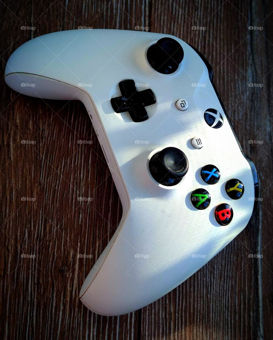 White gaming joystick on a wooden background.  The sun's rays fall on the surface of the joystick