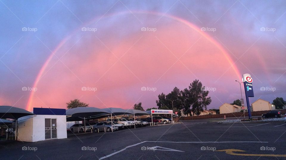 Full colourful rainbow captured over the clouds, cars and homes at a petrol station 