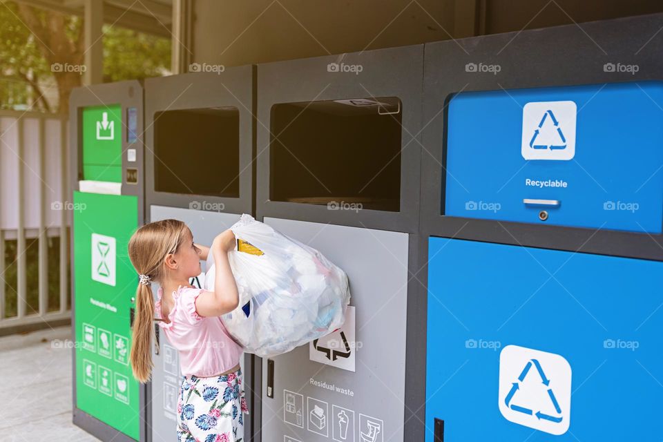 Little Caucasian girl with blonde hair throws sorted garbage into a container for recycling