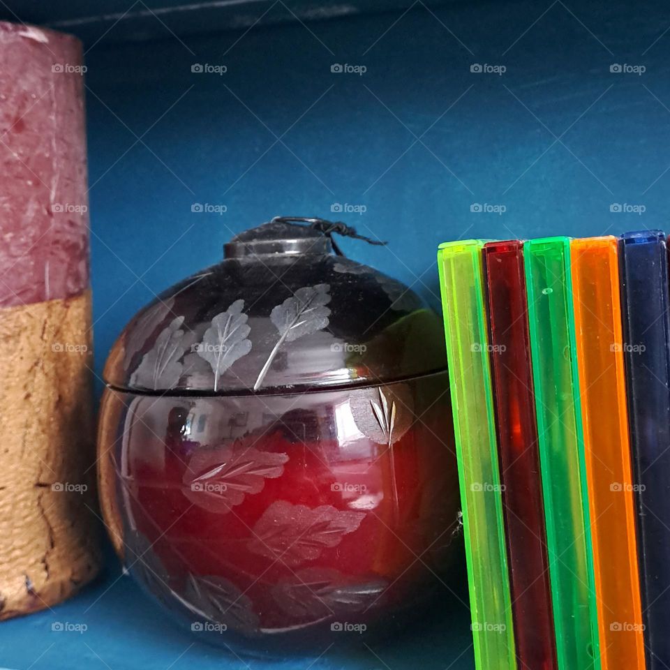 Dark green shelving holding items of autumn colour. burgandy candle holder and bright cd cases