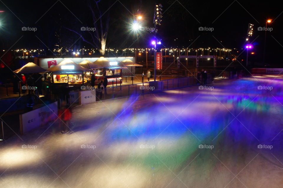 The Vienna ice rink in the evening a long exposure shot with long shadows of people and colourful lighting spots in early spring. People whose faces cannot recognize, skating to the music circle and having fun