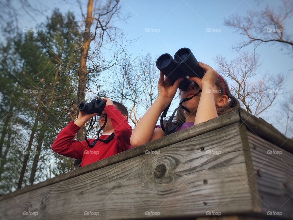 Brother and sister watching through binoculars in forest