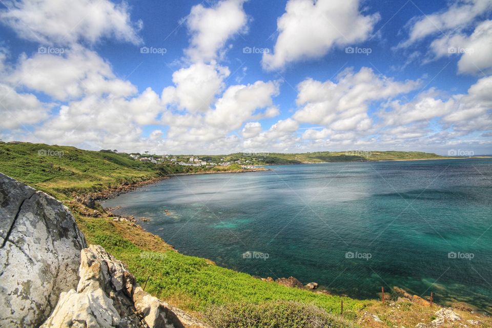 The green shoreline of Cornwall on a bright summer day. Emerald green sea and wide expansive bay.
