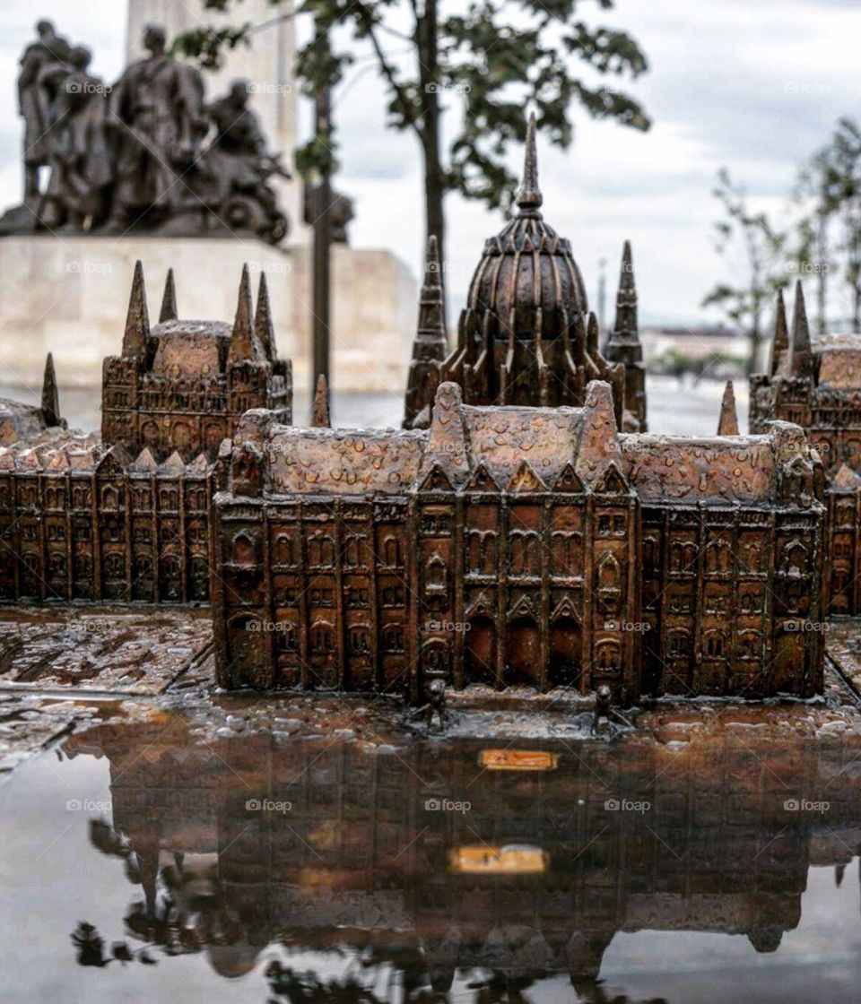 To scale statue of the Hungarian Parliamentary buildings,  enhanced by the reflection of a puddle  