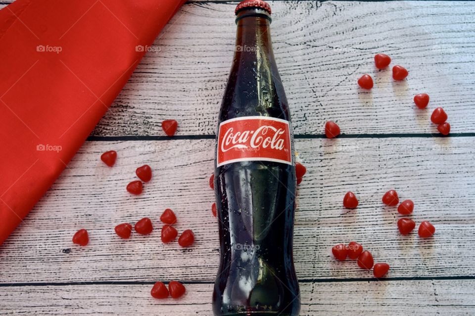 A bottle of Coca-Cola with candy hearts on a white rustic bedroom
