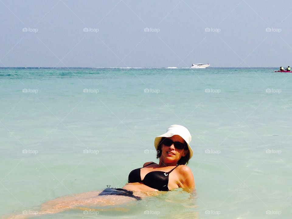 Woman lying in sea wearing hat and sunglasses