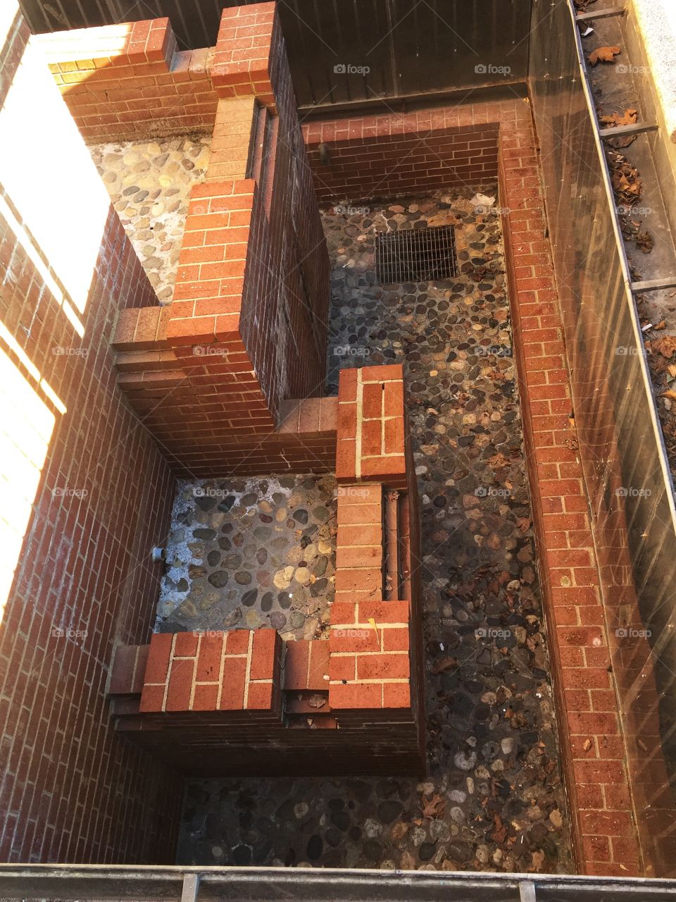A brick work drainage area set in a deep covered with a stone work floor. There is a drainage grill visible.