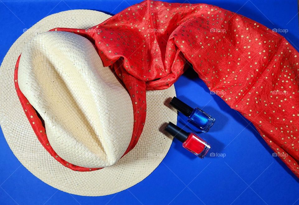 Orange and blue complementary colours flatlay composition on a blue surface with a straw hat, an orange silk scarf and blue and orange nail varnishes