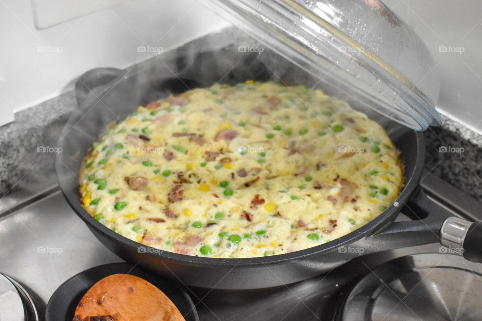 Homecooking cooking Frittata at home and adding and mixing ingredients and removing the Frittata from the pan for cutting and serving on a white plate with tomatoes. Healthy home cooking in kitchen. Breakfast and lunch food preparation.