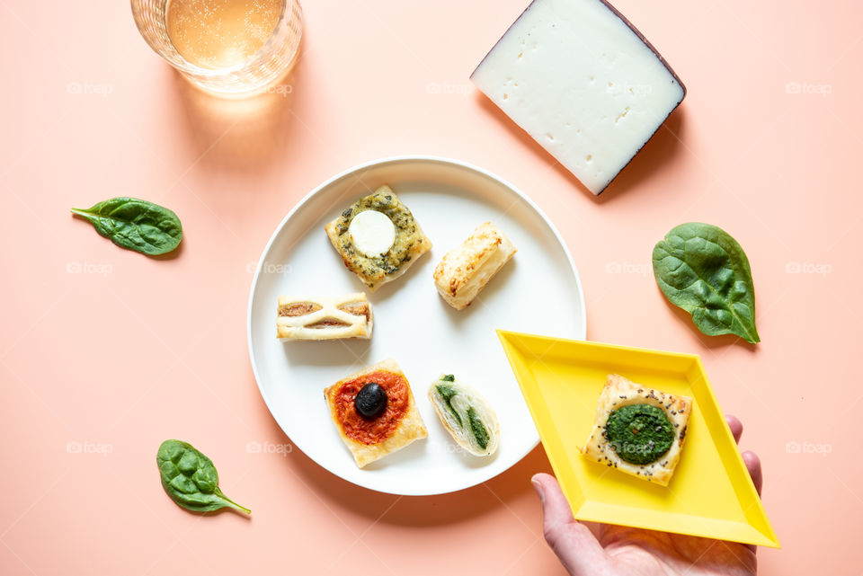Flat lay of a cocktail and appetizers with a person’s hand holding a plate 