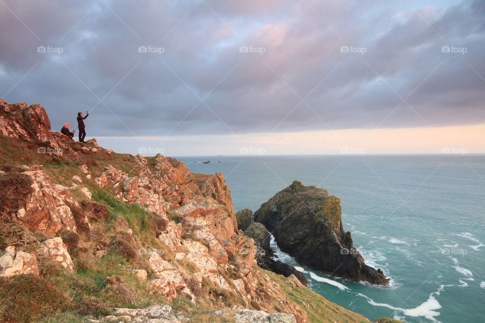 Extreme Selfie. Two people taking selfies on a cliff side while the sun sets over the ocean.