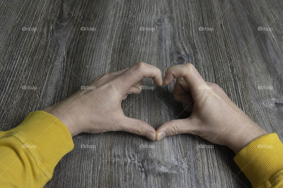 Men's hands folded in the shape of a heart in a yellow jacket lie on a gray wooden surface, which is used as a background or a surface with incident light.