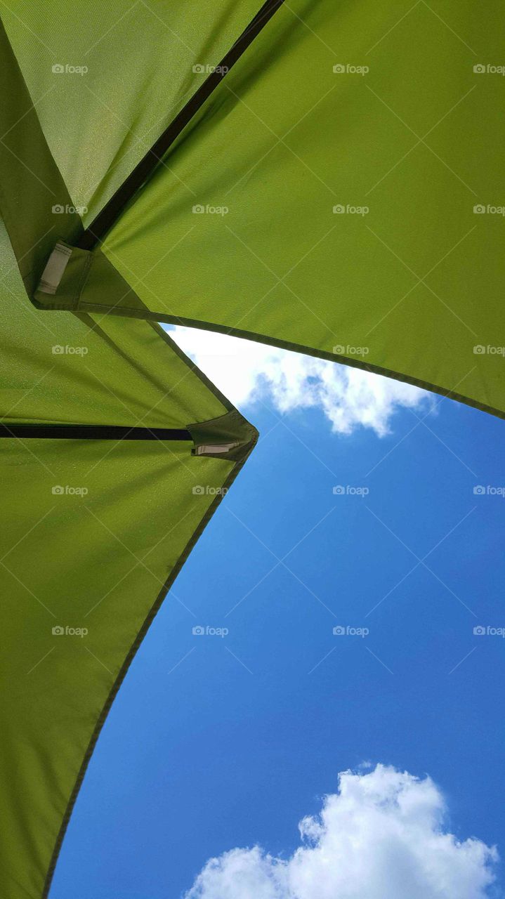 A view of a beautiful summer day looking upward from under beach umbrellas.