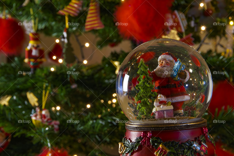 Christmas snow globe ball before blurred background with space for text. 
Decorating Christmas dome ball with Santa Claus before a lit Christmas tree.