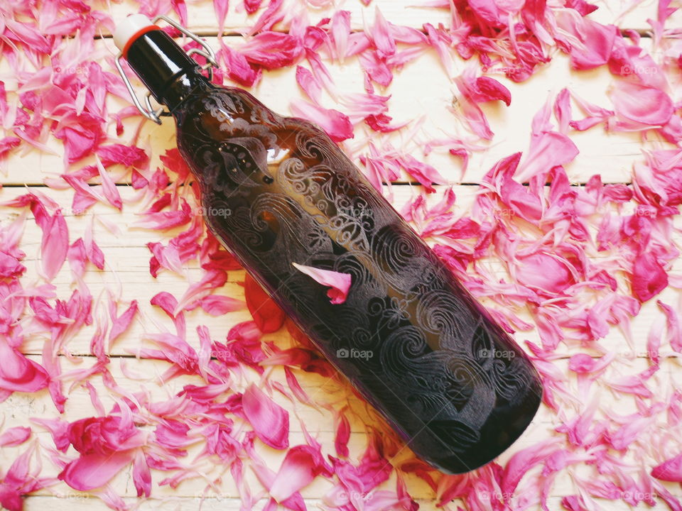 decorative glass bottle and peony flower petals on white background