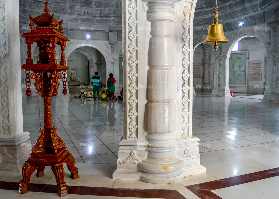 Beautiful Design of Luxury Metallic Lighting Lamp inside Jain temple. White marble sculpture of Jain tirthankara in meditation in a blurry background.