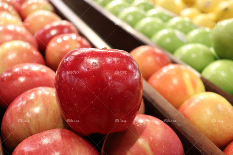 Side view of bright red, small apple with other, differently colored apples in the background. 