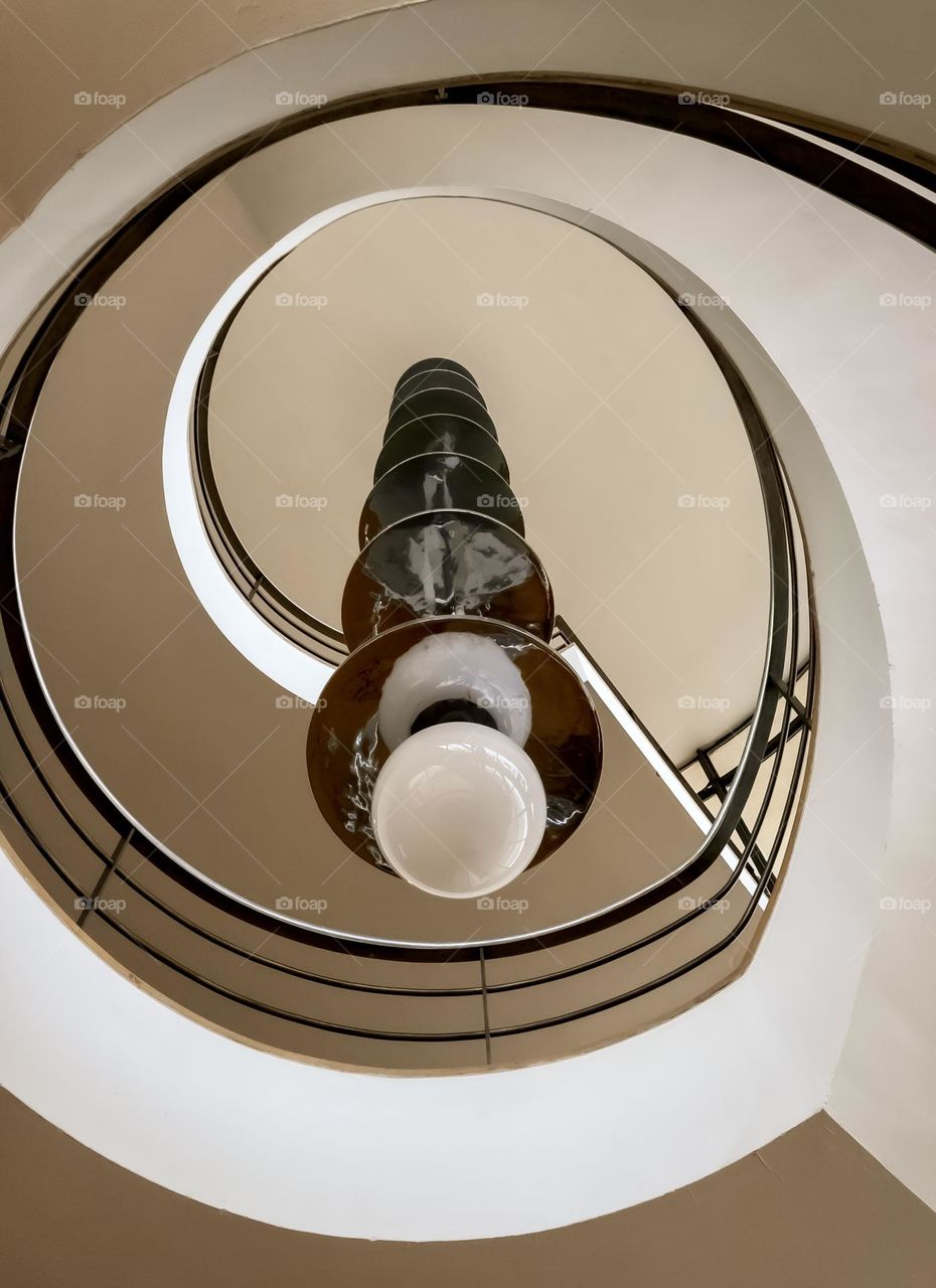 An upwards view through a spiral staircase with circular light hanging through the centre