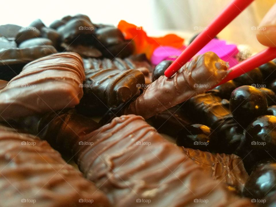 close-up of picking up chocolate toffee with red chopsticks, mixed chocolate candy