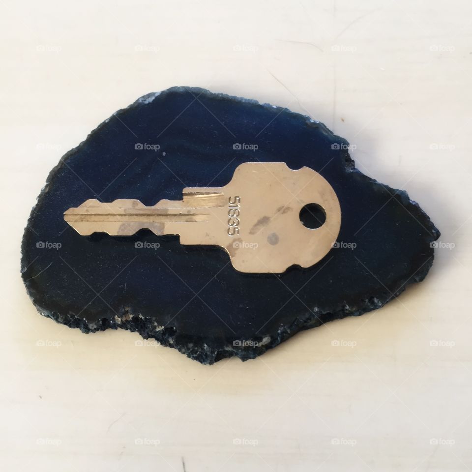 A small key sits on top of a slice of blue geode. It rests on a white background.