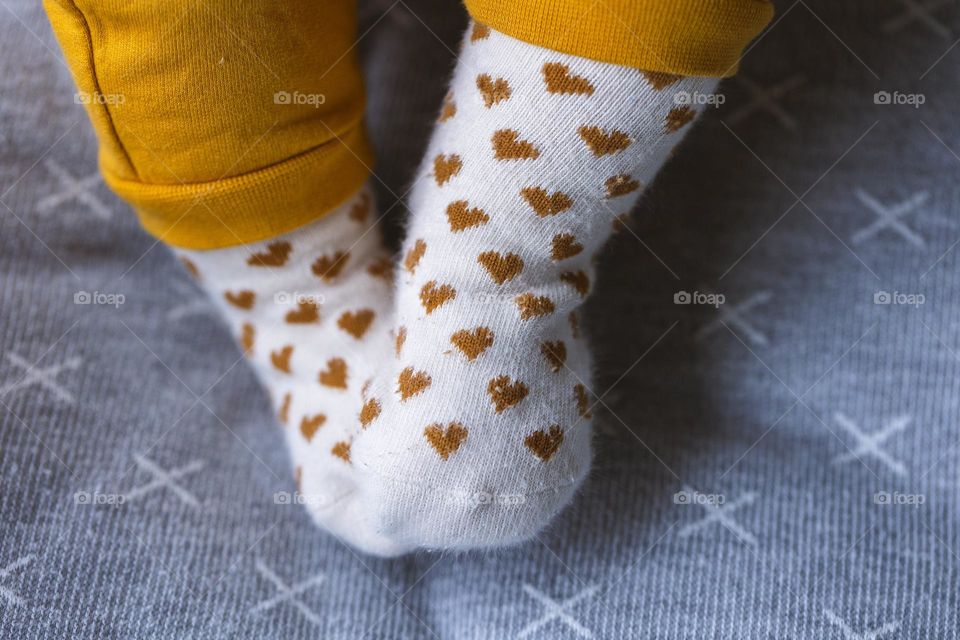 A portrait of tiny cute baby feet in little white socks with brown hearts on them.