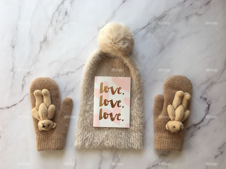 Flat lay items. Winter hat, card with inscription love, mittens lying on marble background 