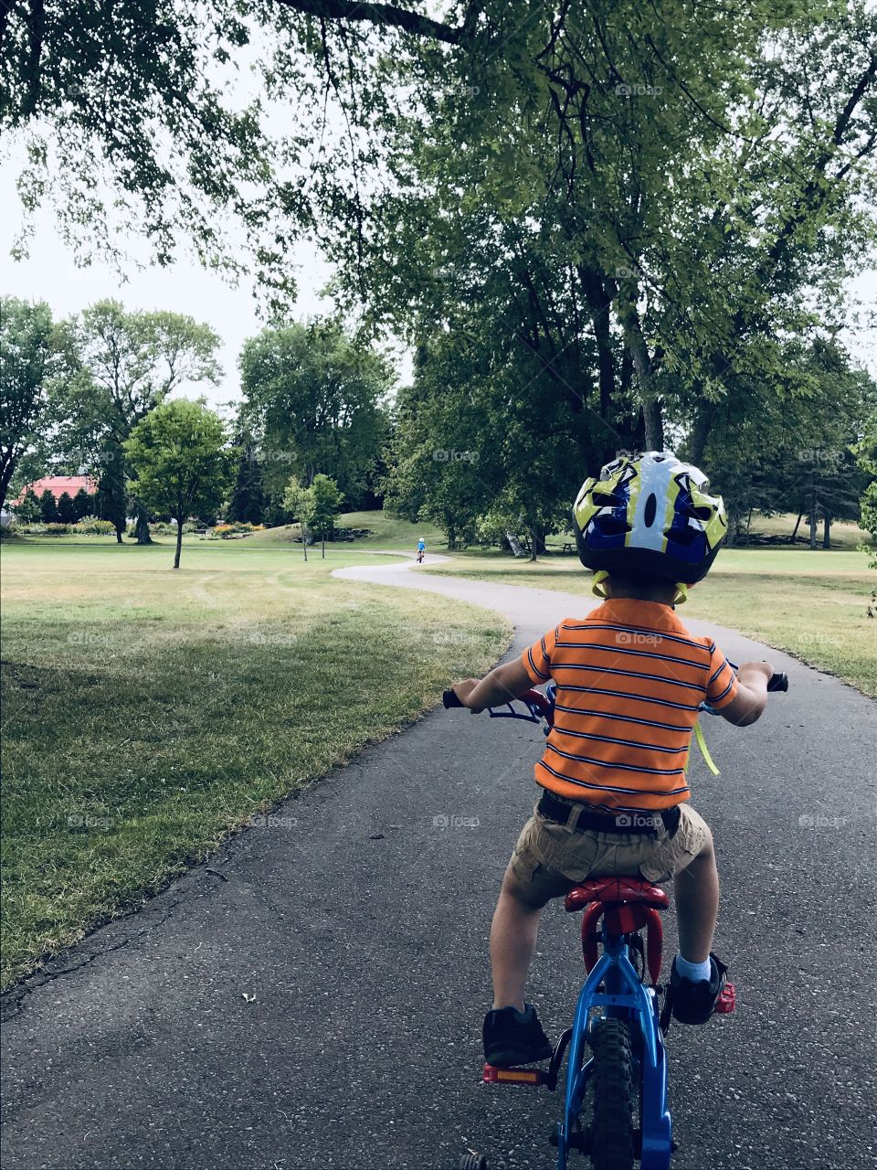 A young boy riding on a bicycle down a path through a park