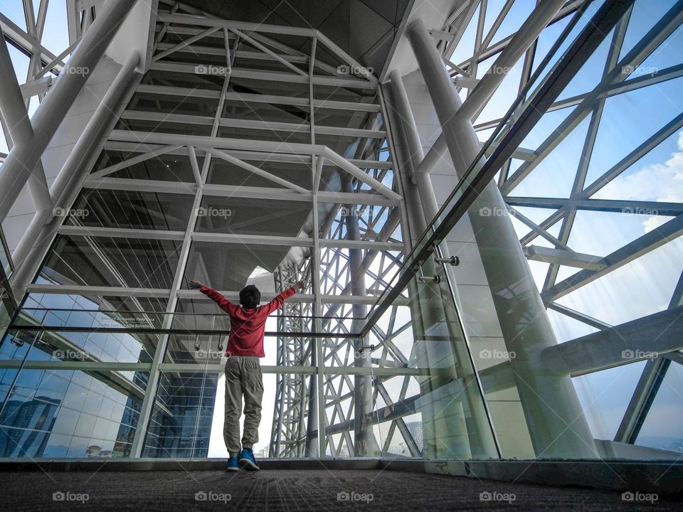 A boy standing against the steel and glass structures